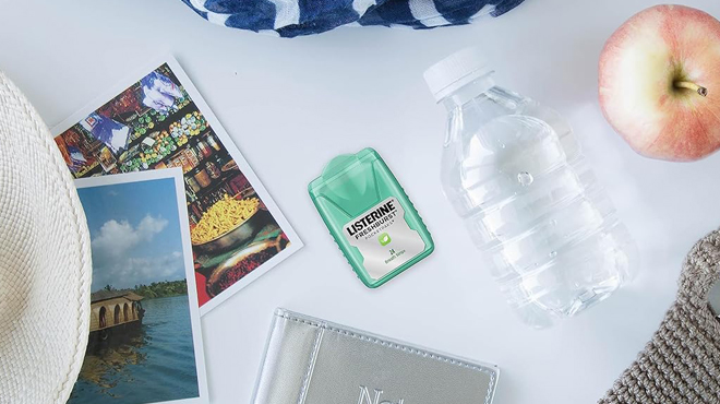 Listerine Breath Strips on a Table Beside an Apple a Water Bottle and Pictures