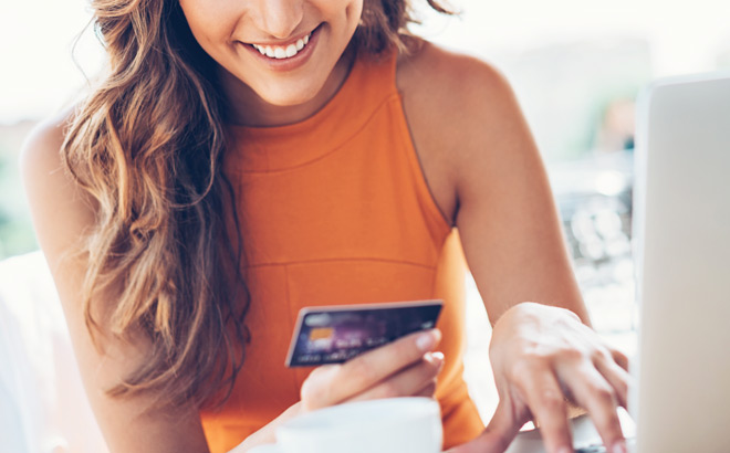 A Person Typing on a Laptop While Holding a Credit Card and Smiling