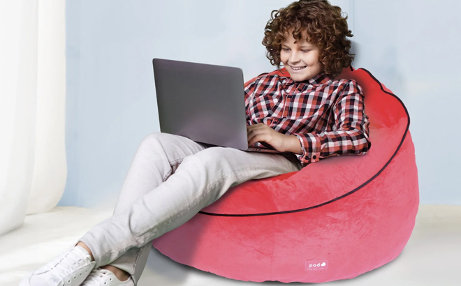 A kid seated on a Marvel Spiderman Kids Bean Bag Chair while using a laptop