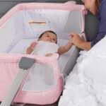 A lady cuddling a baby lying inside a Skylar Bassinet and Bedside Sleeper