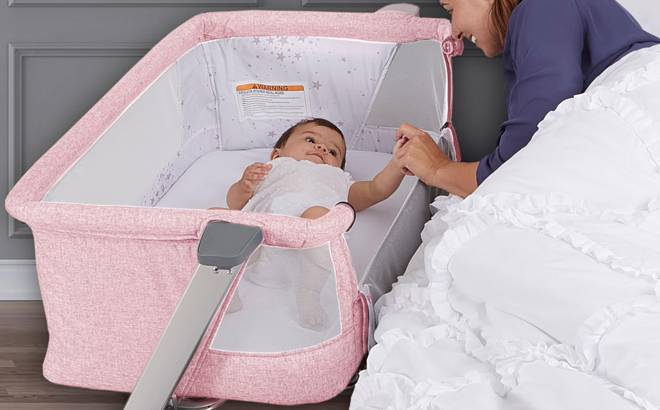 A lady cuddling a baby lying inside a Skylar Bassinet and Bedside Sleeper