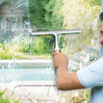 A person cleaning a window using a Scrubit Window and Shower Squeegee