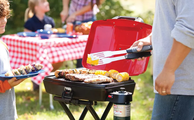 A person grilling meat on Coleman Sportster Propane Grill