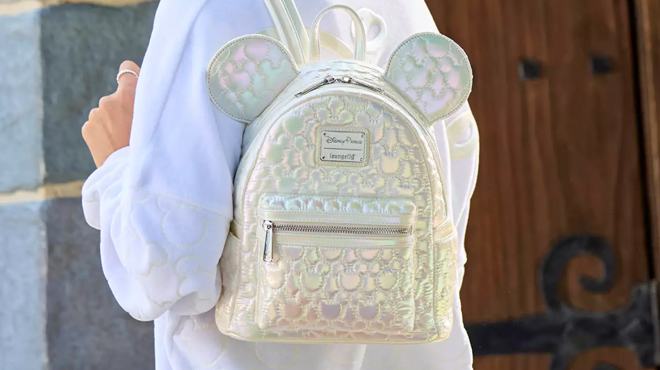 A person slinging a Mickey Mouse Icon Quilted Iridescent Loungefly Mini Backpack