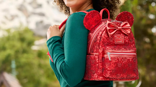 A person slinging a Minnie Mouse Red Sequin Loungefly Mini Backpack