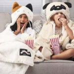 A Girl and a Boy in Squishmallows Hooded Throws Sitting on the Sofa and Eating Popcorn