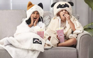 A Girl and a Boy in Squishmallows Hooded Throws Sitting on the Sofa and Eating Popcorn