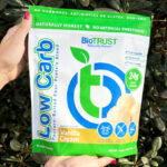 A Woman Holding a Bag of BioTrust Low Carb Protein with Green Leaves in the Background