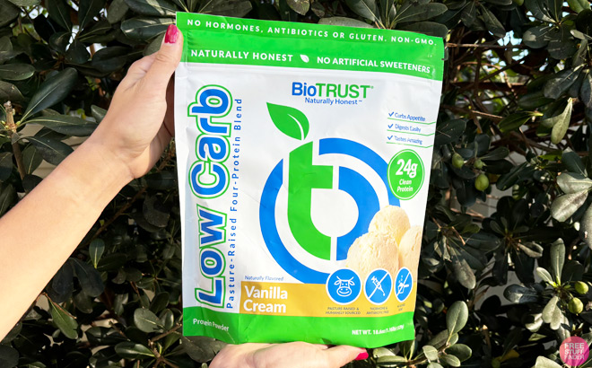 A Woman Holding a Bag of BioTrust Low Carb Protein with Green Leaves in the Background