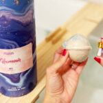 A Woman Holding a Forever Fizzies Bath Bomb and a Vial with a Diamond Inside