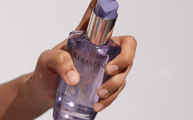 A hand holding a Kerastase Hair Oil