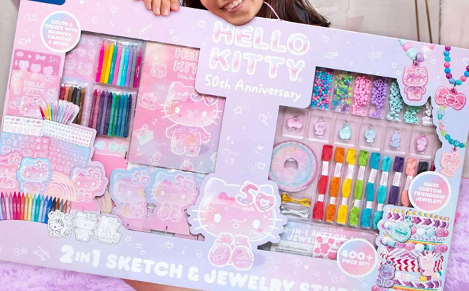 A Girl Sitting on the Floor and Holding a Hello Kitty 50th Anniversary Sketch Jewelry Studio Set