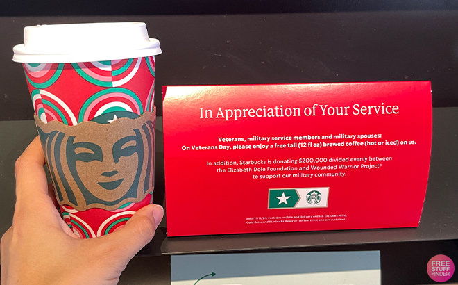 A Person Holding a Starbucks Cup Next to a Veterans Day Starbucks Offer Sign