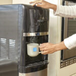 A Person Using Primo Deluxe Bottom Load Black and Stainless Water Dispenser