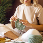 A Smiling Woman Sitting on a Bed and Crocheting