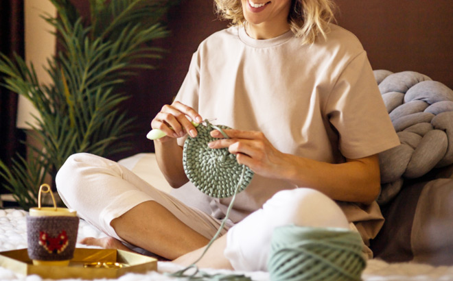 A Smiling Woman Sitting on a Bed and Crocheting