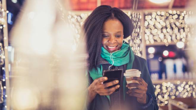 A Smiling Woman in a Holiday Setting Holding a Phone and a Coffee Cup