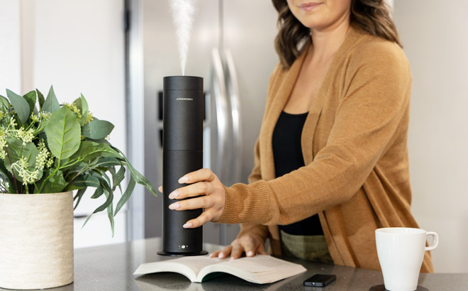 A Woman Putting an Aroma360 Mini Pro Scent Diffuser on a Table next to a Book