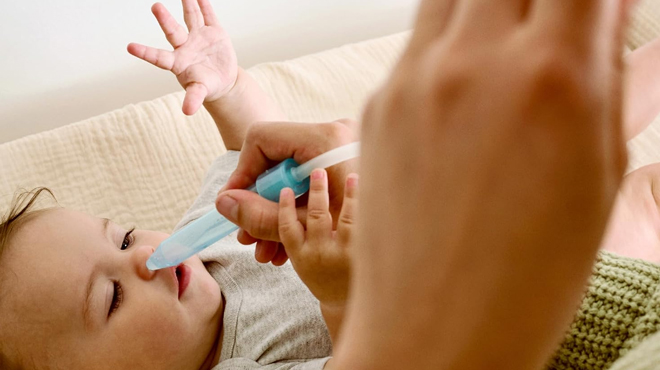 A parent using a Frida Baby SnotSucker Nasal Aspirator to help her baby