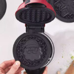 A person holding a Dash MultiMaker™ Mini System Holiday Waffle Maker with Removable Plates