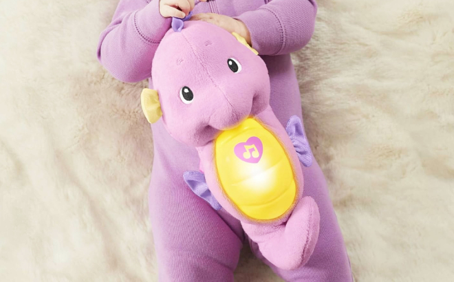 A Baby Holding a Fisher Price Musical Plush Baby Toy