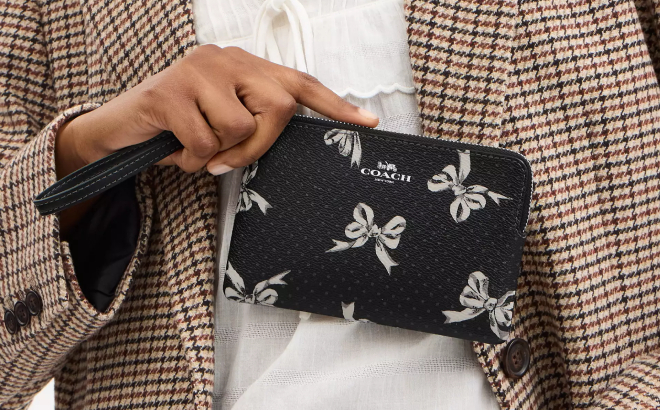 A Person Holding a Coach Outlet Corner Zip Wristlet With Bow Print