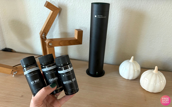 A Woman Holding Three Oils with the Hotel Collection Studio Pro Scent Diffuser in the Background