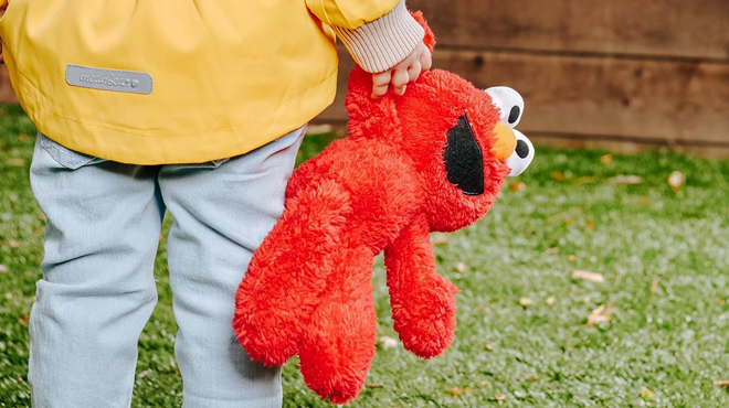 A child holding a Sesame Street 13 inch Elmo Plush Toy