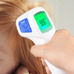 A person measuring the temperature of a child using a Berrcom Non Contact Forehead Thermometer