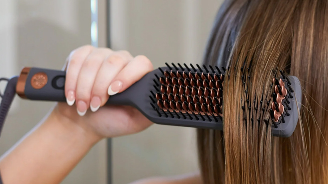 A person using a Hairitage Ceramic Hair Straightener Brush to brish her hair