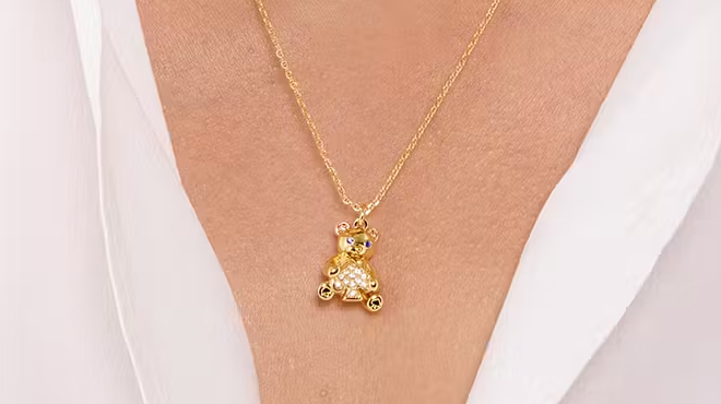 A person wearing a necklace with a Kate Spade Teddy Bear Pendant