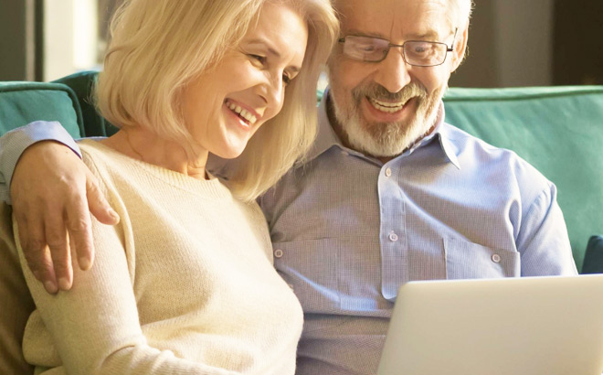 An Elderly Couple Smiling and Looking at a Laptop to Maximize Their Savings