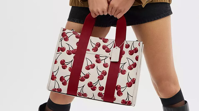 A lady carrying a Coach Outlet Smith Tote Bag With Cherry Print