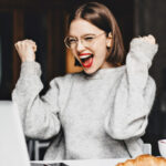 Ecstatic Young Woman Looking at Her Laptop and Making Yes Gesture